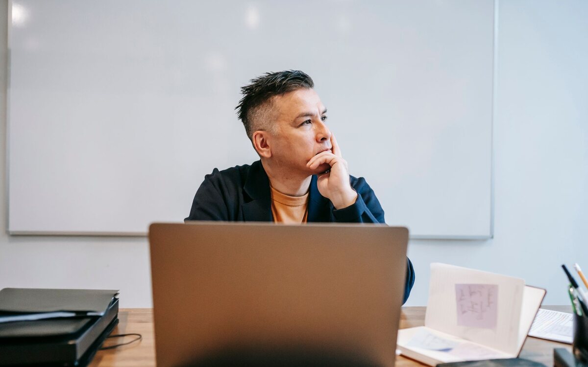 Homem diante do notebook, pensativo, em sua mesa de trabalho